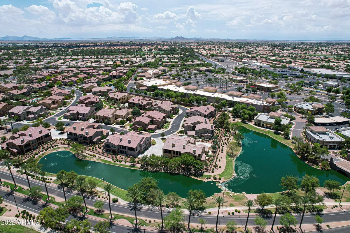 A serene water body is bordered by meticulously landscaped grounds and rows of attractive houses. Walking paths wind along the water, inviting outdoor activity and community interaction in a peaceful setting.