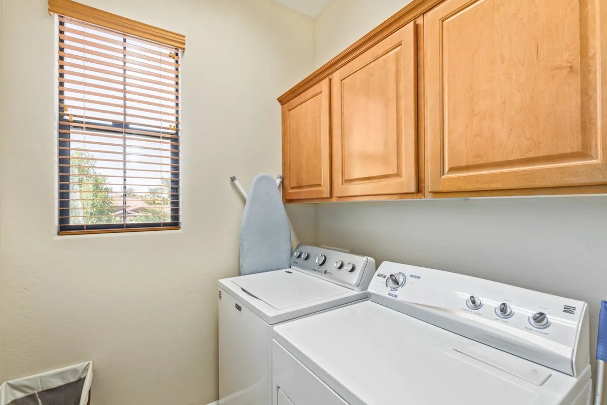 A practical laundry room with a washer, dryer, wooden cabinets, and an ironing board. The space is tidy and well-lit, showcasing its convenience and utility for guests planning longer stays.