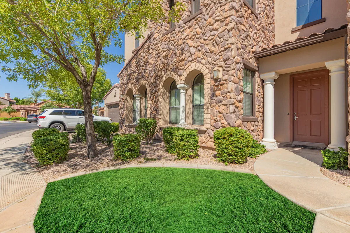 A welcoming exterior featuring a stone facade, arched windows, and a landscaped front yard. Families are gathered by the entrance, with hints of outdoor relaxation and socializing in the sunshine.