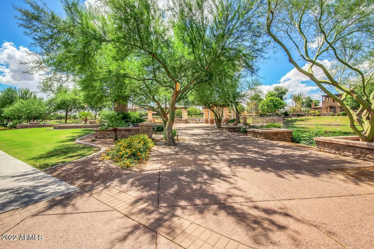 A beautifully landscaped outdoor space with a neatly paved path, flowering shrubs, mature trees, and stone walls. The inviting walking trail winds through lush greenery, epitomizing resort-style community spaces.
