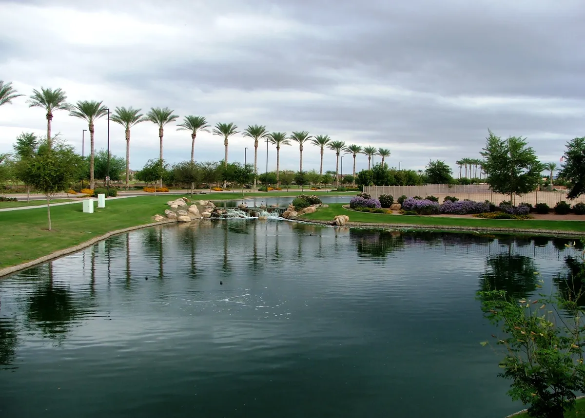 A tranquil pond is accented by a gentle waterfall, framed by palm trees and colorful flower beds. The lush landscaping creates a serene setting perfect for unwinding or enjoying a leisurely stroll, evoking the calming atmosphere of a high-end golf course environment.