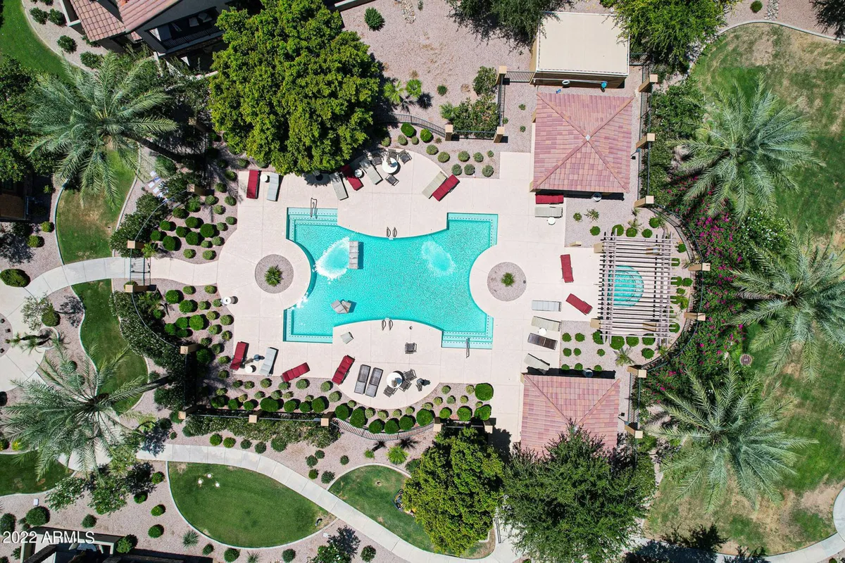 A tranquil swimming pool area with lounging chairs, a hot tub, shaded pergola, and lush greenery surrounding the space. The image captures both the pool and spa, with ample room for socializing and relaxing.