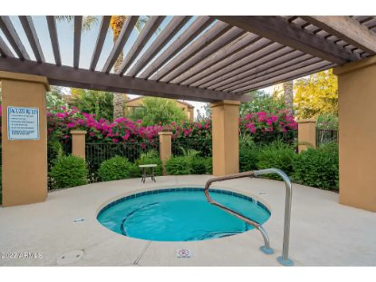 A tranquil hot tub sits under a charming pergola, surrounded by flowering plants and dappled sunlight. The space is designed for relaxation and socializing, with a touch of lush landscaping creating a private oasis feel. The scene suggests comfort and rejuvenation after a day of activity.