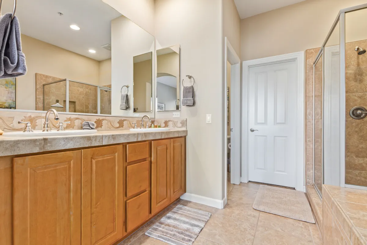 A stylish bathroom with a double vanity, large mirrors, and a glass-enclosed shower. The space is bathed in soft, tranquil lighting, and features spa-like finishes that evoke relaxation and self-care.