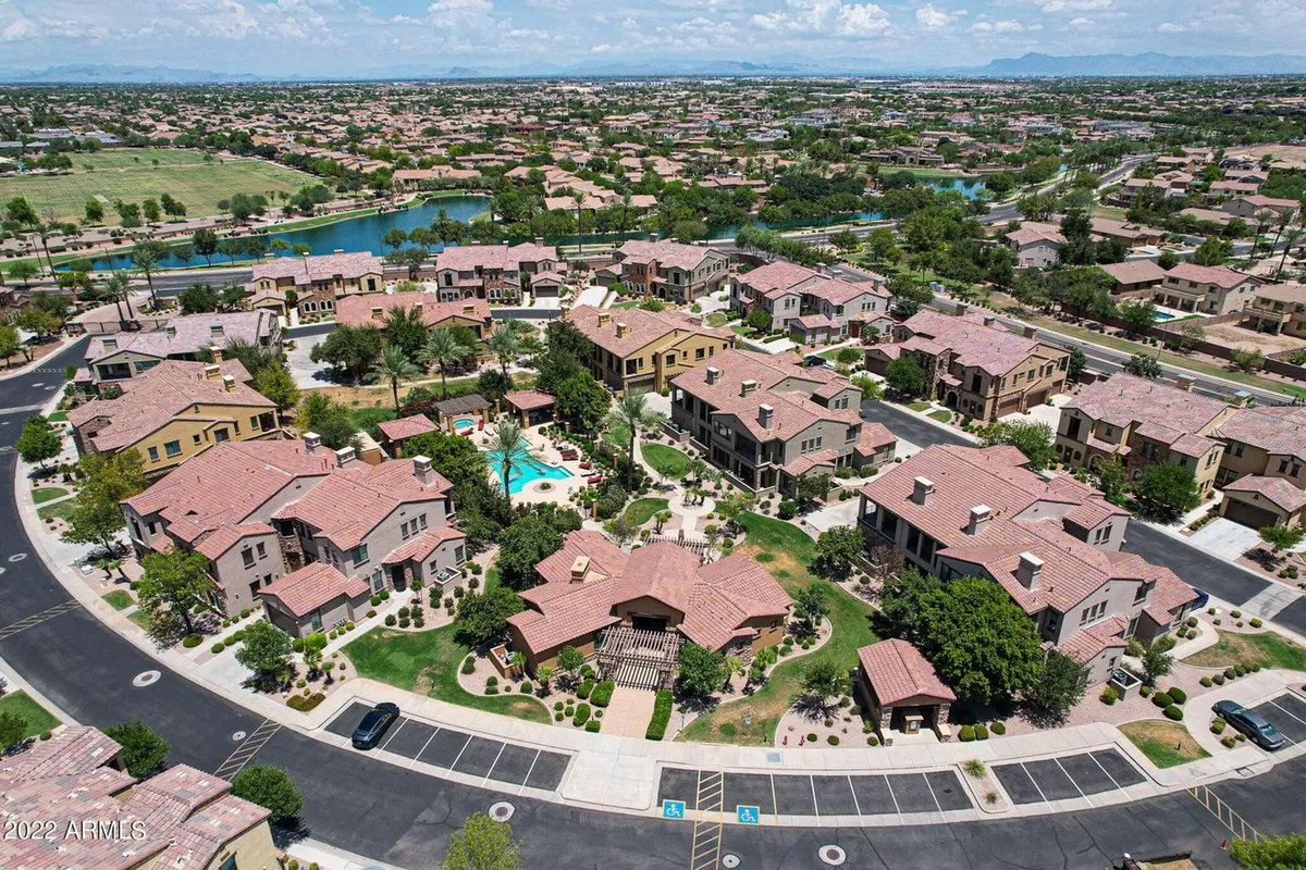 A vibrant community pool surrounded by landscaped gardens, walking paths, and a tranquil lake view in the background. The space is set up for gatherings, with lounge chairs and colorful umbrellas, evoking a sense of community and outdoor enjoyment.