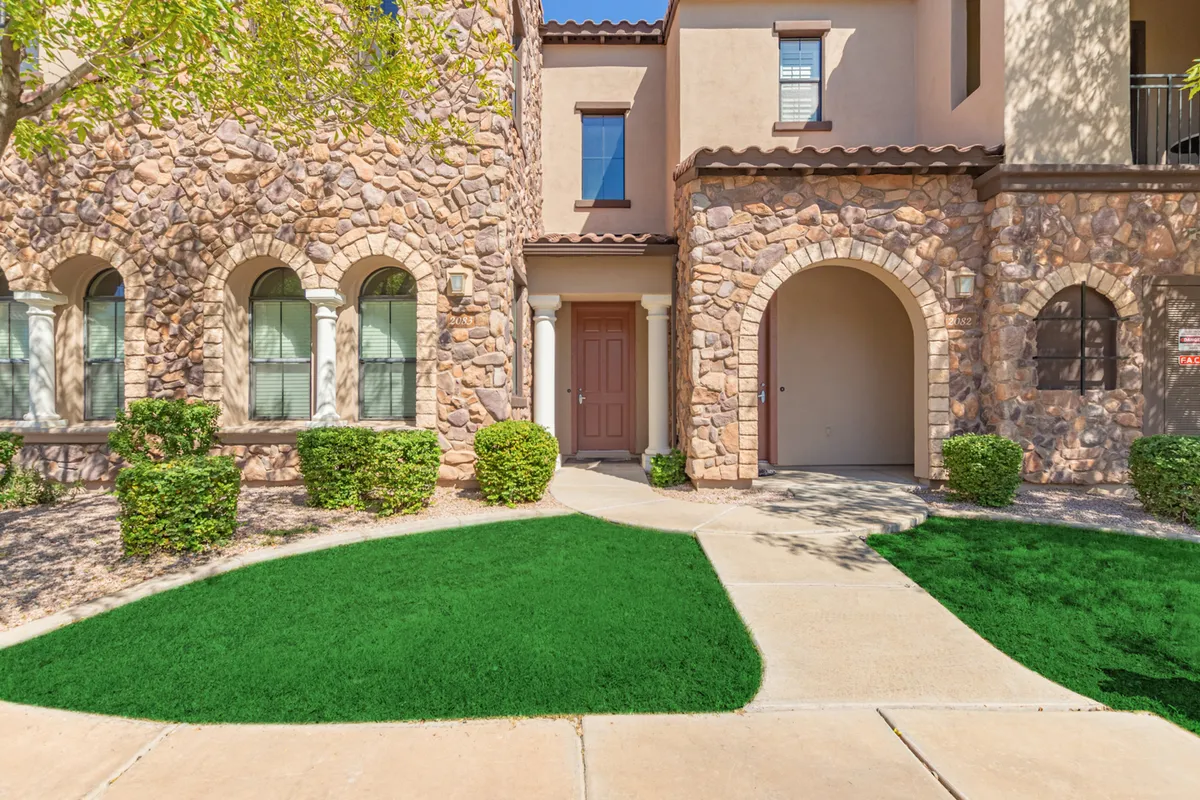 A view of the property’s textured stone facade and symmetrical windows, with an arched entryway and manicured green lawn. Residents are seen greeting guests at the inviting entrance, highlighting a welcoming community atmosphere.
